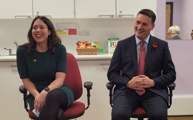 Alice Macdonald sitting next to Wes Streeting. They are sat in a doctors surgery and both smiling.